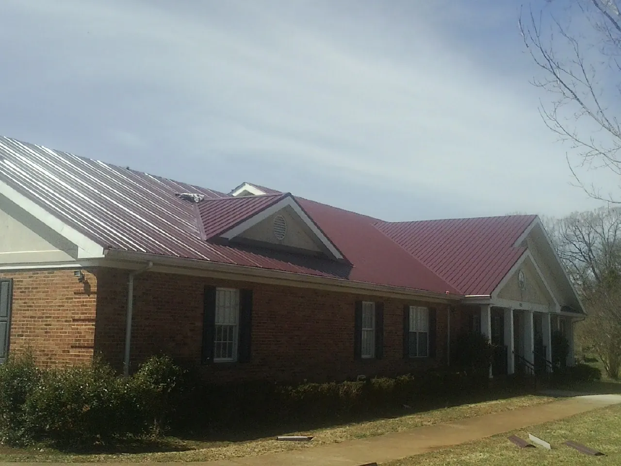 Red metal roof with gabled entries on a long brick building, from a Hail Damage Roof Repair job in Somersworth