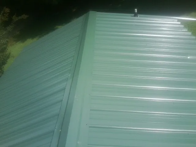 New green metal panels meeting at the ridge of a roof — Flat Roof Repair work by our crew in Somersworth