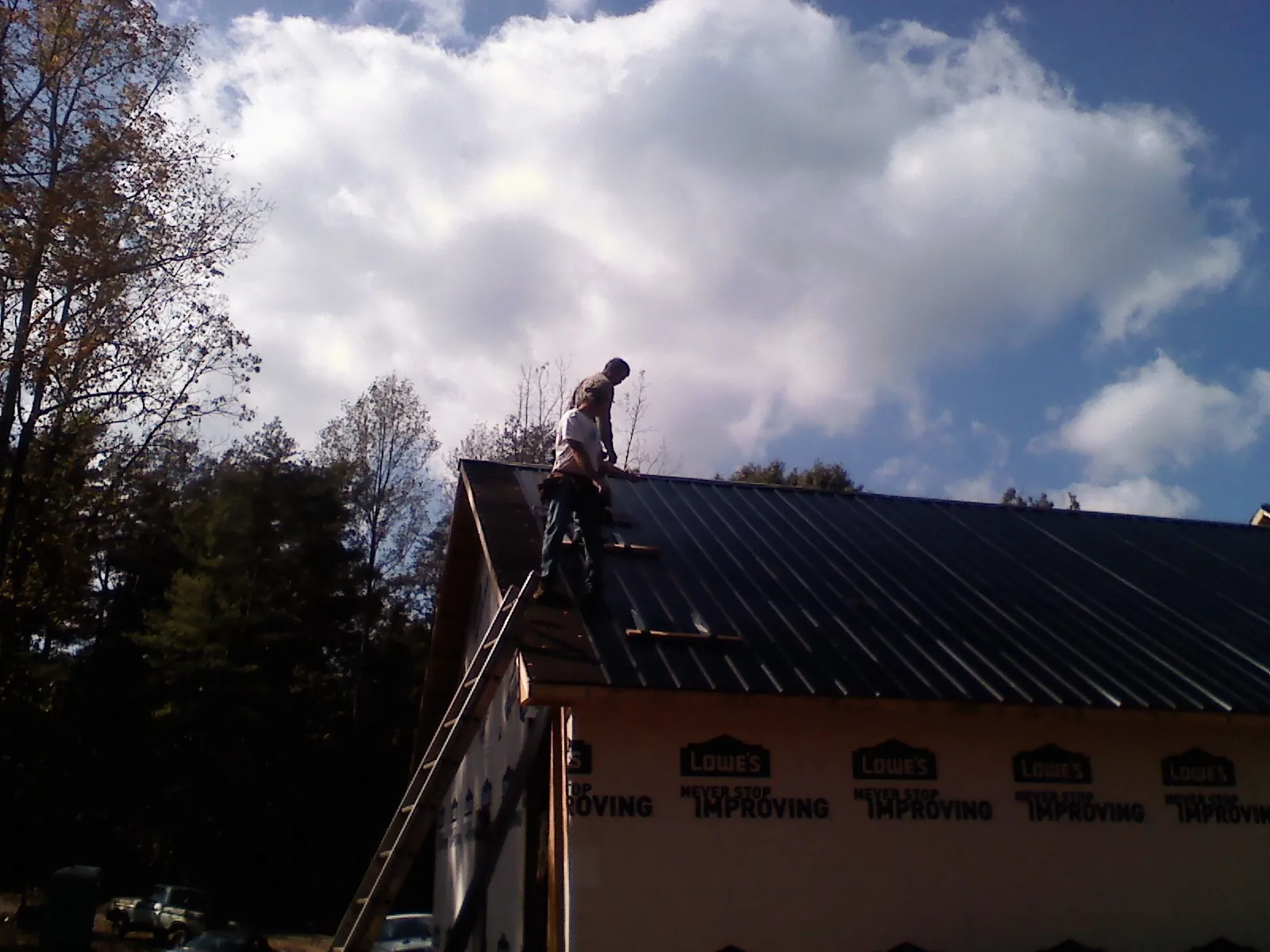 Roofer fastening dark metal panels high against a cloudy sky, from a Roof Inspection job in Somersworth
