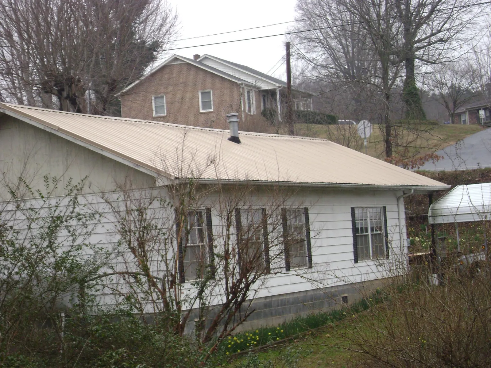 Tan metal roof on a white sided house set into a hillside — Commercial Roofing by Roofing Brothers in Somersworth