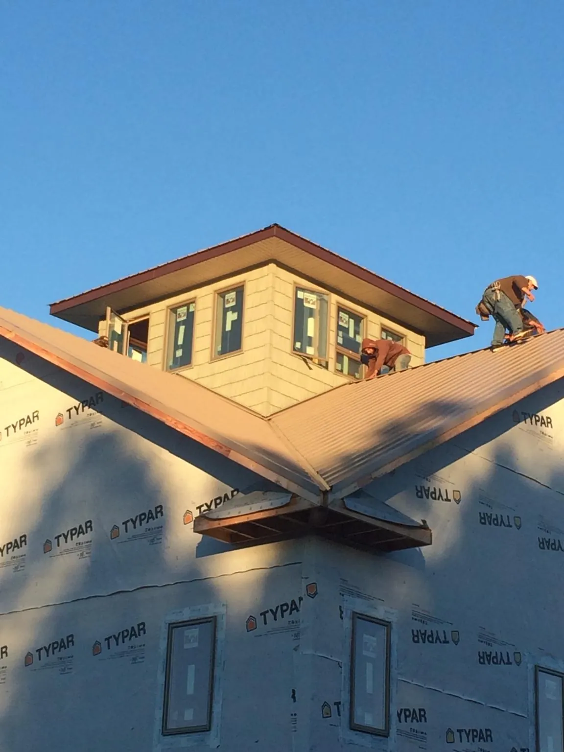 Roofers working around a rooftop cupola on a new metal roof at sunset — Roof Waterproofing in Somersworth by Roofing Brothers
